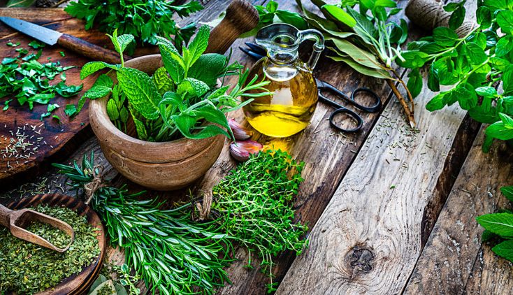 A wooden table covered in herbs, plant clippings, and a bottle of pesticide.