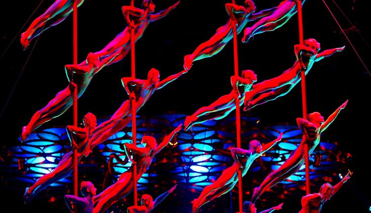 Acrobats performing on stage with red and blue lights shining on them.