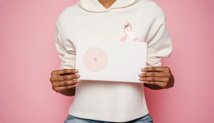 A woman in a white sweater holding up an illustration of a breast.